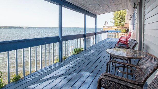 A wooden deck with a railing overlooking a body of water, featuring wicker furniture and a table.