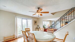 A dining area with a glass-top table, wooden chairs, and a ceiling fan. - Rooftop Deck & Hot Tub: Outer Banks Family Getaway (Rodanthe)