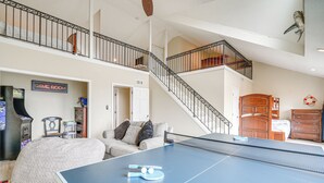A spacious living area with a ping pong table, a couch, and a staircase leading to an upper level. - Rooftop Deck & Hot Tub: Outer Banks Family Getaway (Rodanthe)