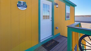 A yellow building with a white door, a welcome mat, and a sign that says "Come Gather on Our Porch". - 9 Mi to Lake Carlsbad: Pet-Friendly Apt (Carlsbad)