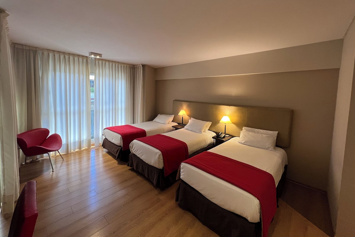 A hotel room with three beds, a desk, and a chair.