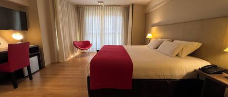 A hotel room with a large bed, a desk with a chair, a TV, and a phone on the nightstand.