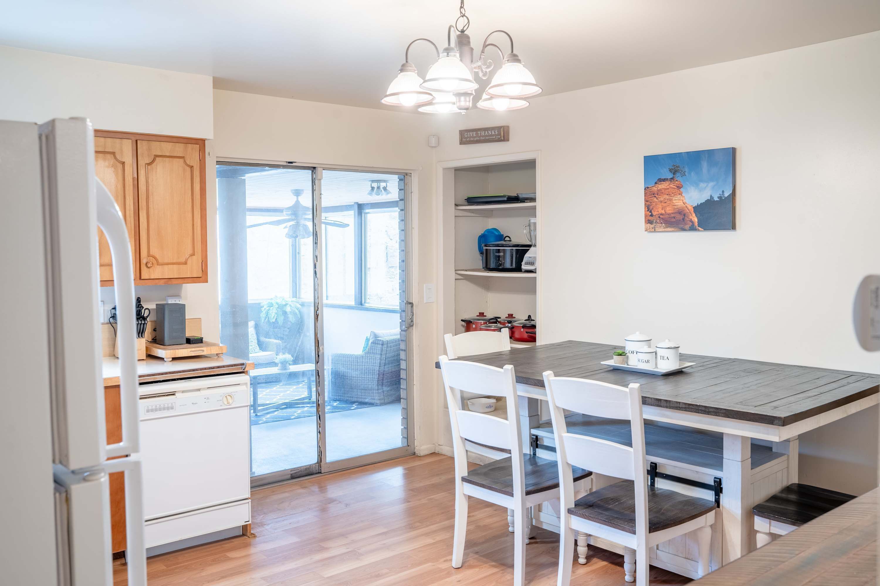 A kitchen with a wooden table, white chairs, a refrigerator, and a window.