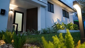 A modern house with a well-lit entrance, a wooden door, and a small garden area with plants and a pathway. - Spacious 4-bedroom house in Miami with Hot Tub, Lake, Kayaks, and Pool table (Miami)