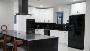 A modern kitchen with white cabinets, a black refrigerator, and a central island with bar stools. - Spacious 4-bedroom house in Miami with Hot Tub, Lake, Kayaks, and Pool table (Miami)