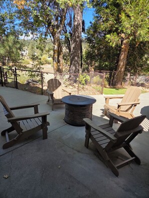 An outdoor patio with Adirondack chairs, a stone fire pit, and a view of a forested area. - Arrowbear Lakehouse, Large Private 5BR-3BA, Deck, Sauna, Media/Game Rm (Running Springs)
