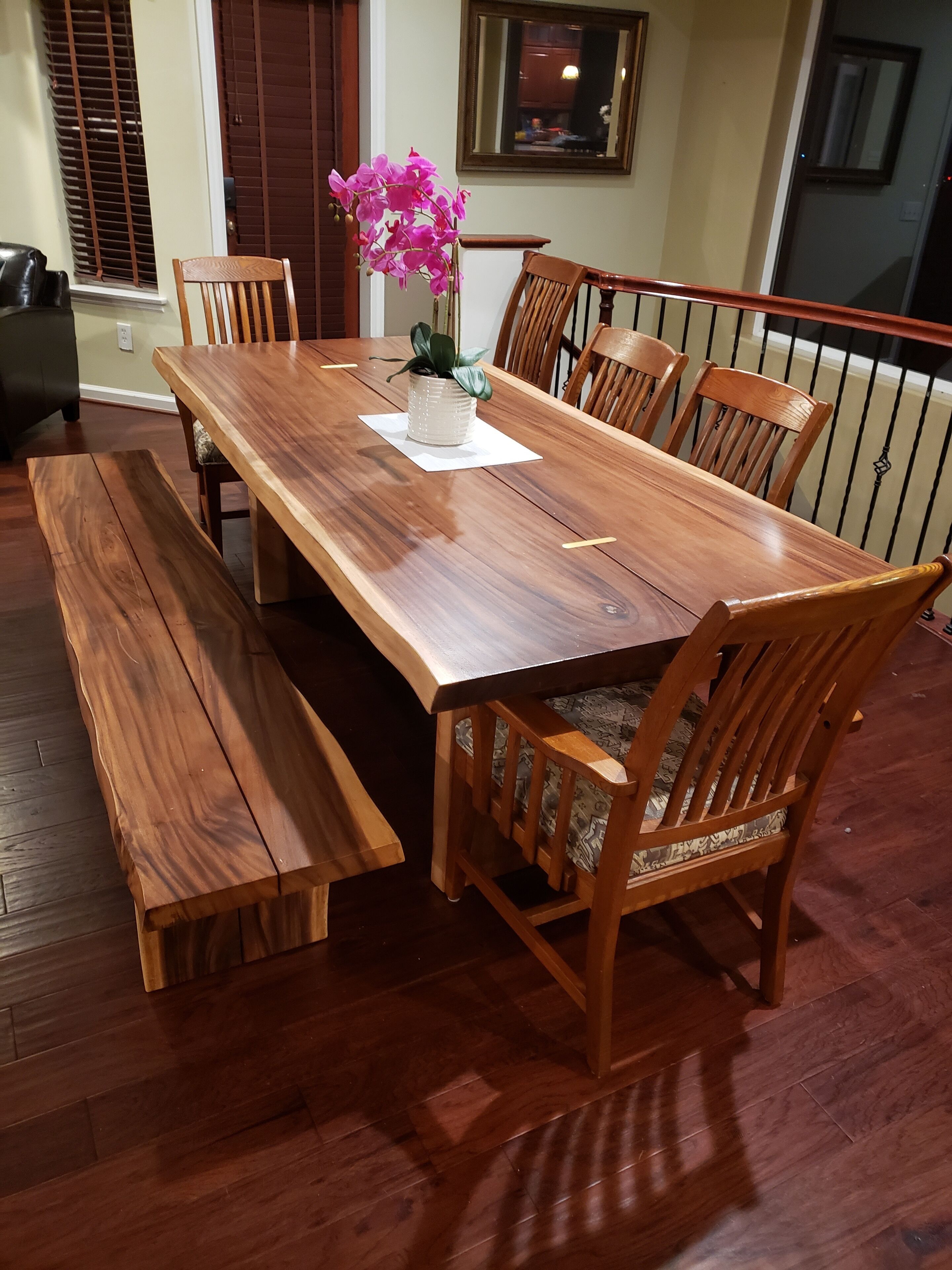 Une table de salle à manger en bois, accompagnée de six chaises, d’un banc et d’une orchidée en pot.