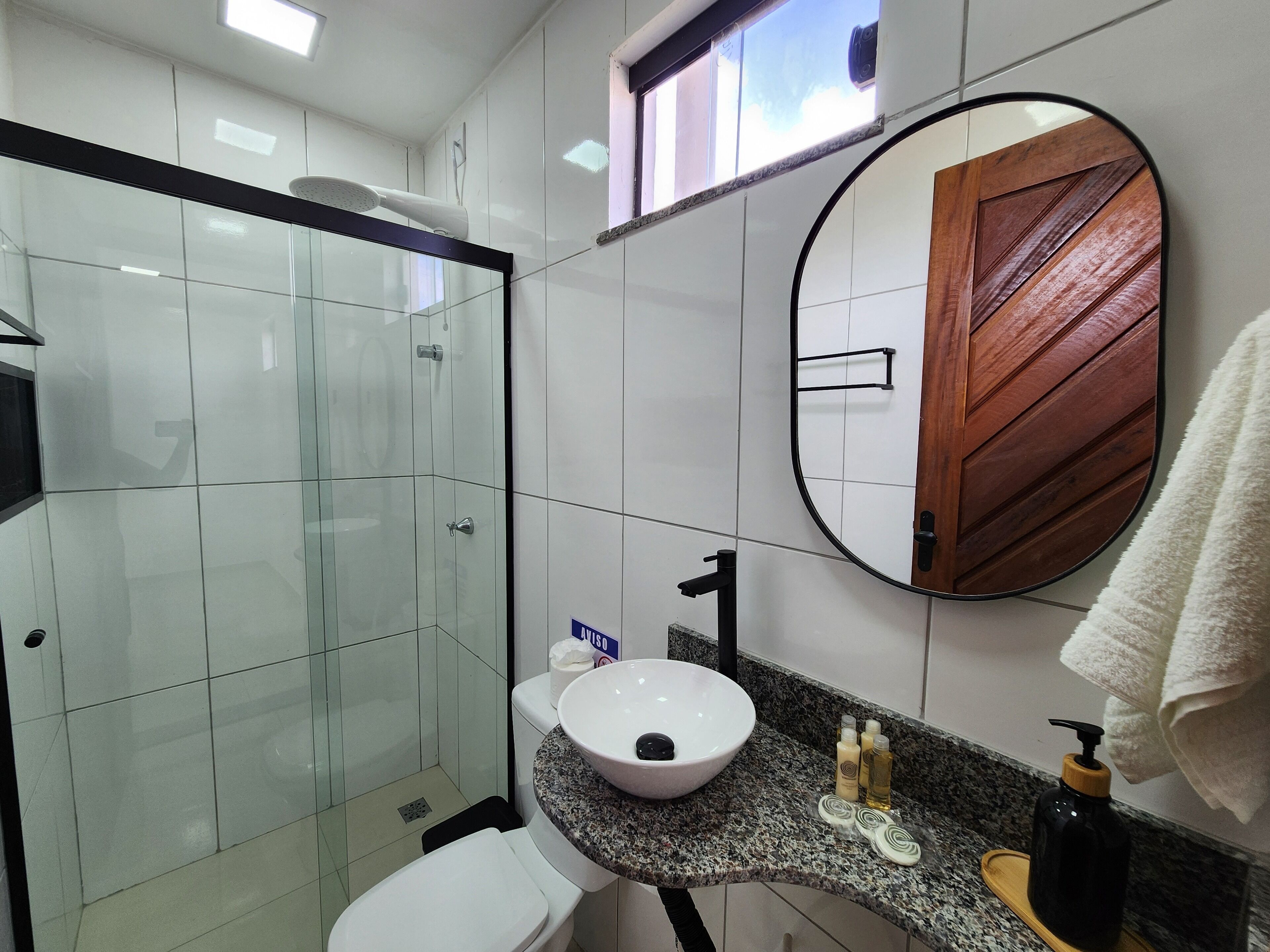 A modern bathroom with a glass shower enclosure, a white sink with a wooden vanity, and a mirror with a wooden door reflection.