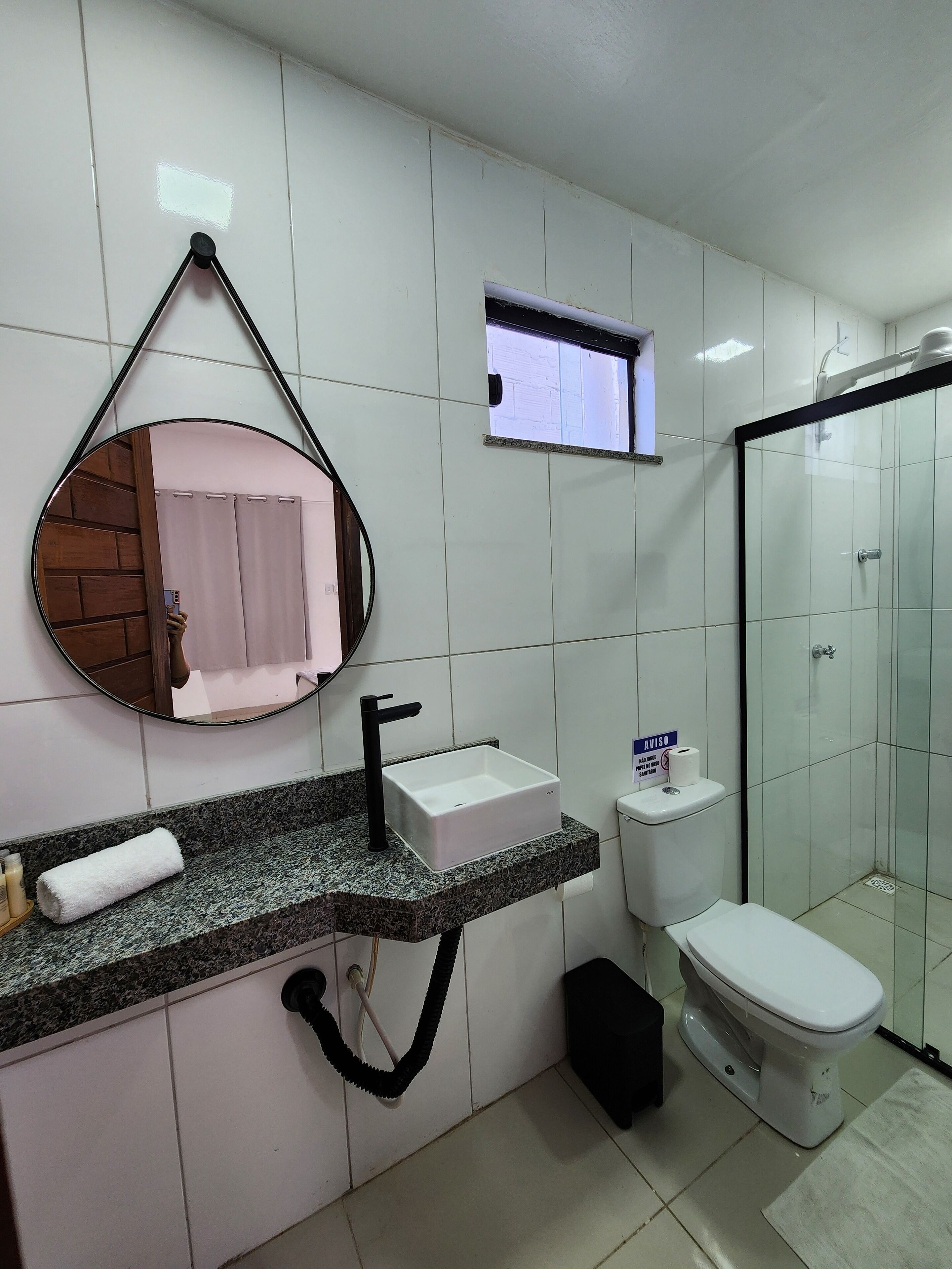 A modern bathroom with a granite countertop, a round mirror, a white sink, a toilet, and a glass shower enclosure.