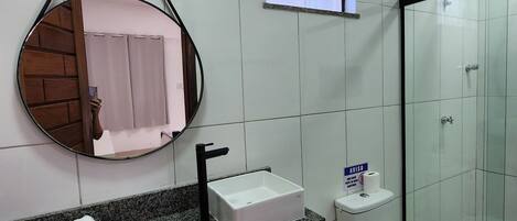 A modern bathroom with a granite countertop, a round mirror, a white sink, a toilet, and a glass shower enclosure.