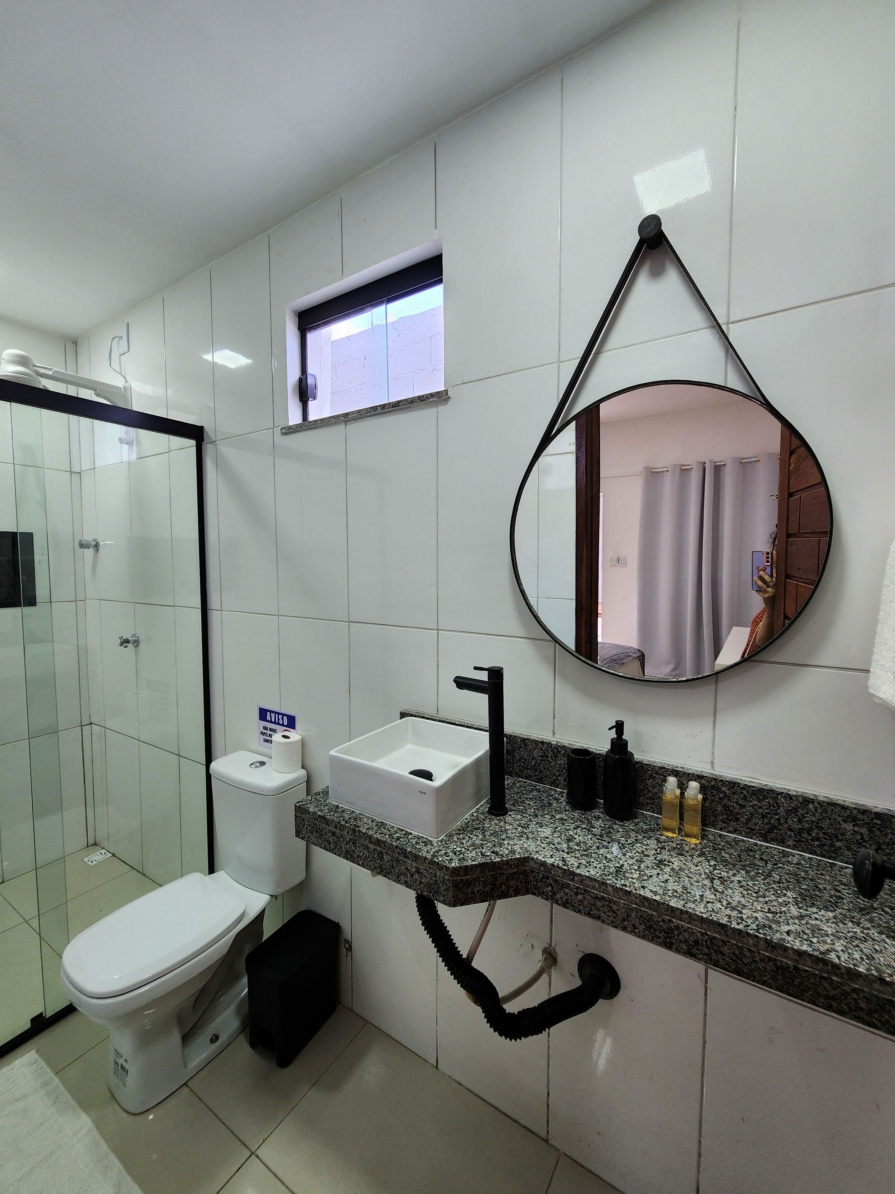 A modern bathroom with a white toilet, a sink with a black faucet, a mirror, and a shower area.