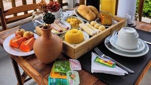 Una mesa de desayuno con diversos alimentos, un florero con flores secas y vista a la playa y al cielo.