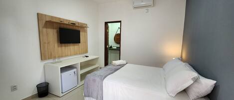 Habitación de hotel con cama, un escritorio pequeño con televisor, un refrigerador compacto y un cesto de basura.