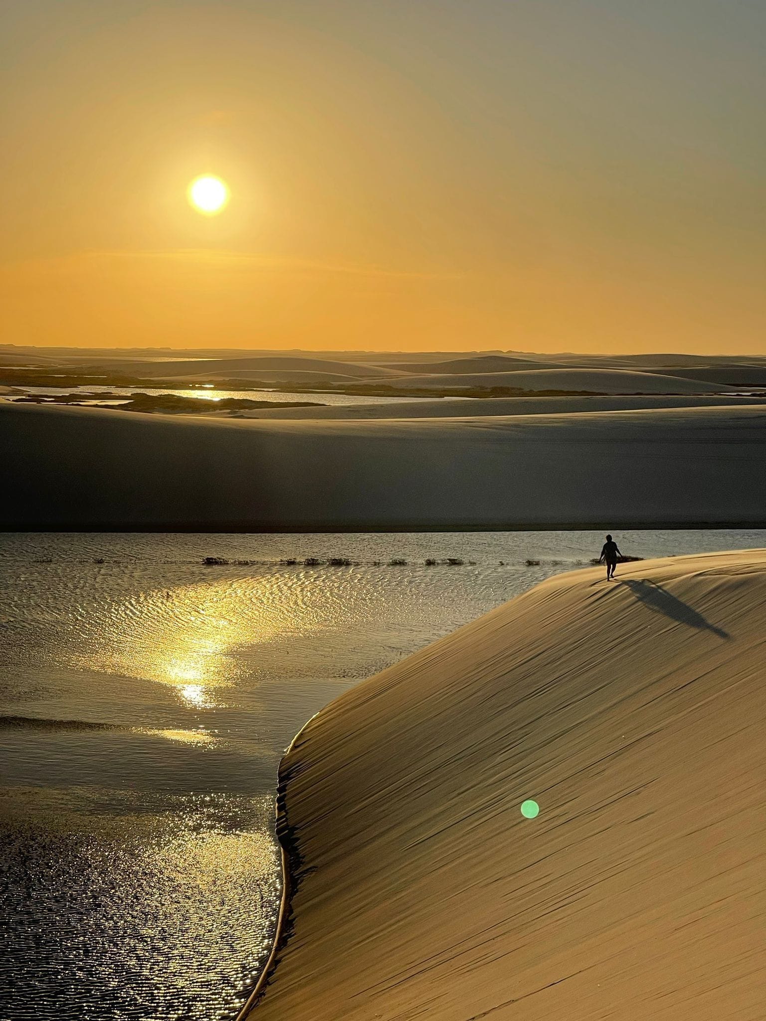 A desert landscape with sand dunes and a person walking on the sand.
