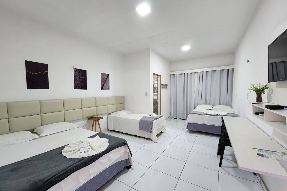 Habitación de hotel con dos camas, un escritorio, una silla, un televisor y una mesita con un jarrón de flores.