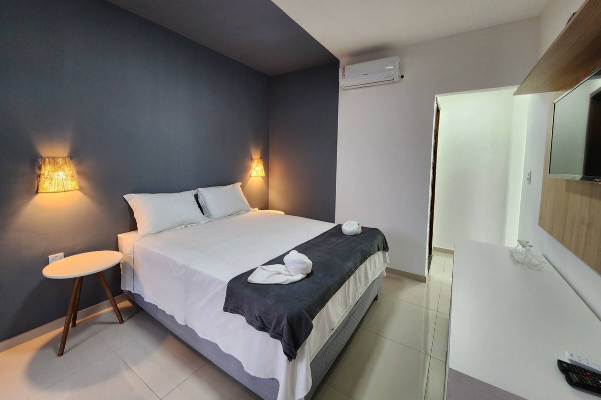 Habitación de hotel con cama, lámparas de noche, una mesa redonda, un espejo y un equipo de aire acondicionado.
