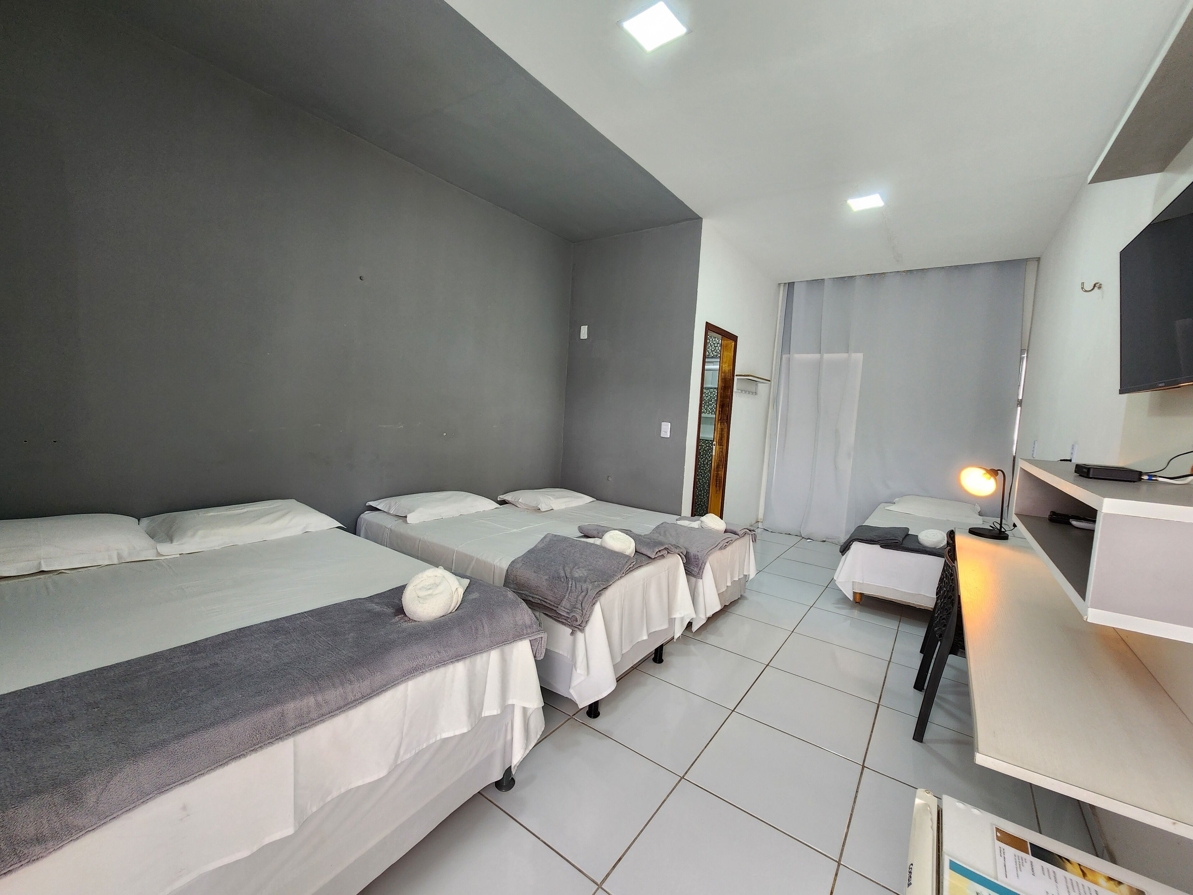 A hotel room with three single beds, a desk with a computer, and a TV.