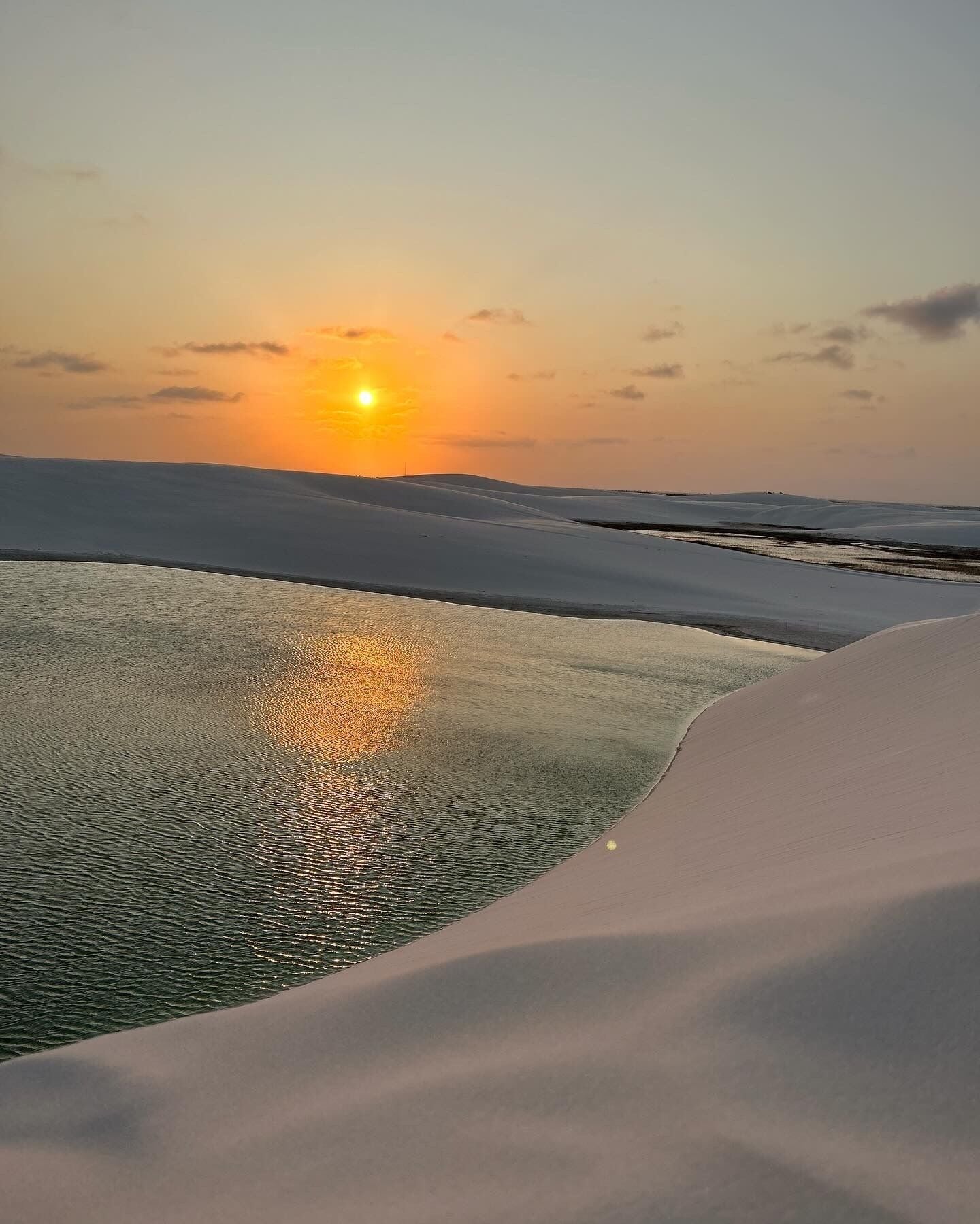 Paesaggio desertico con dune di sabbia e uno specchio d'acqua che riflette il tramonto.