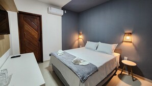 Un dormitorio con cama, lámparas de noche, un escritorio con un control remoto y un aire acondicionado.