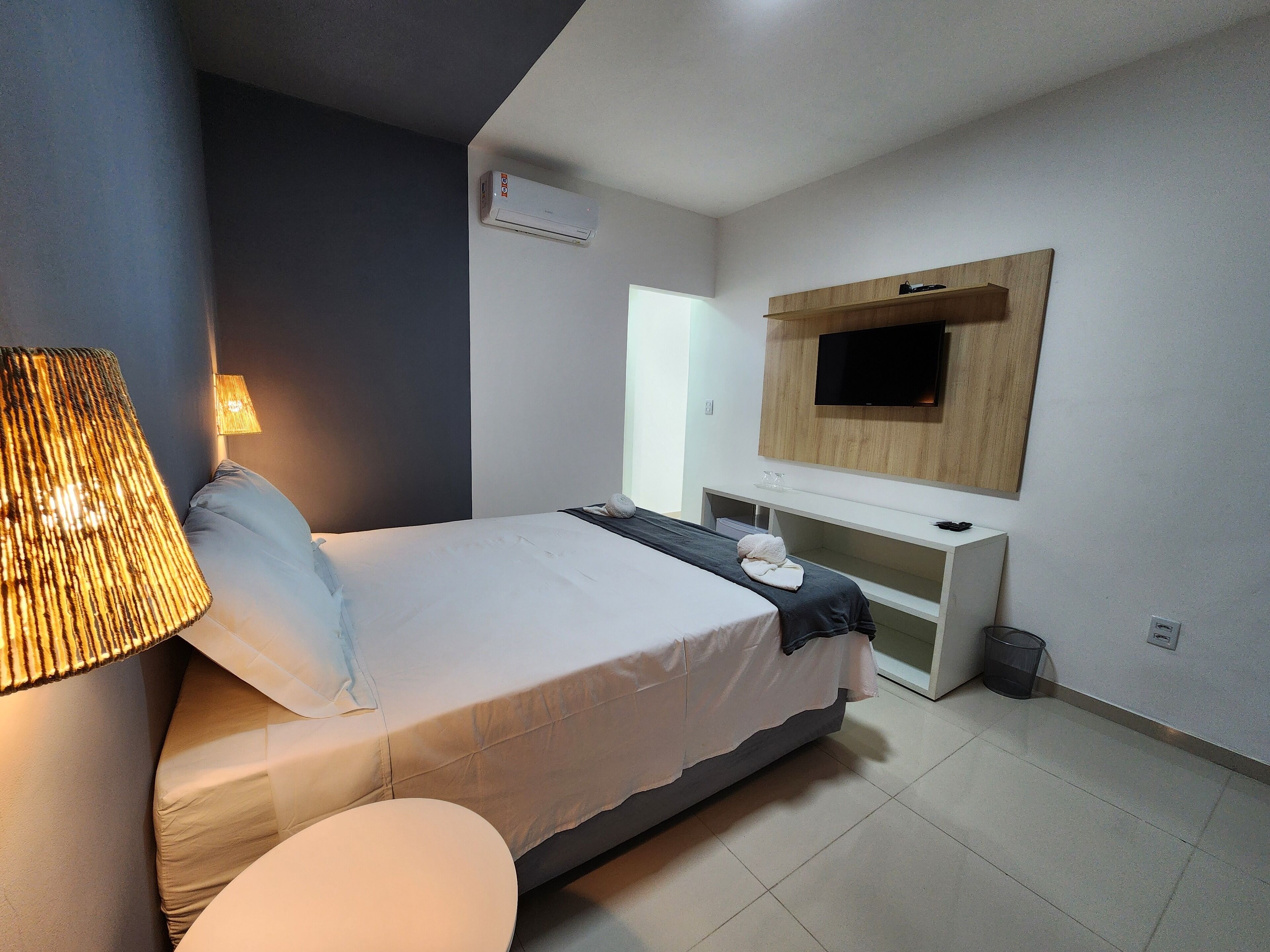 Una habitación de hotel moderna con una cama, lámpara de noche, televisor y un pequeño escritorio.