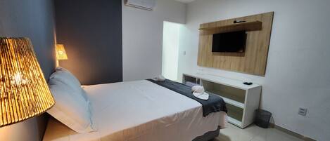 Una habitación de hotel moderna con una cama, lámpara de noche, televisor y un pequeño escritorio.
