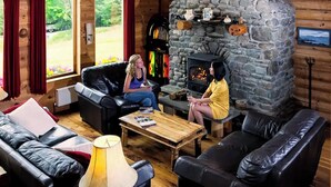 A cozy log cabin interior with a stone fireplace, leather sofas, and a wooden coffee table.