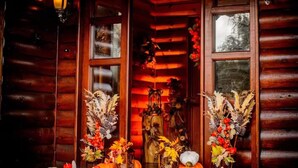 A wooden cabin with a porch decorated with pumpkins and autumn flowers.