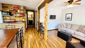 Un vaste espace de vie doté d’un plancher en bois, d’une table à manger avec des chaises, d’un canapé et d’un téléviseur fixé au mur.