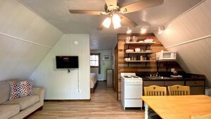 Un espacio habitable compacto con kitchenette, comedor y televisor montado en la pared.