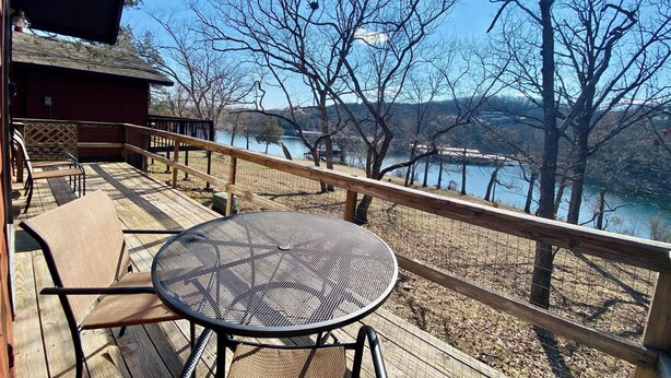 Terraza de madera con mesa y sillas, con vistas a un lago y árboles.