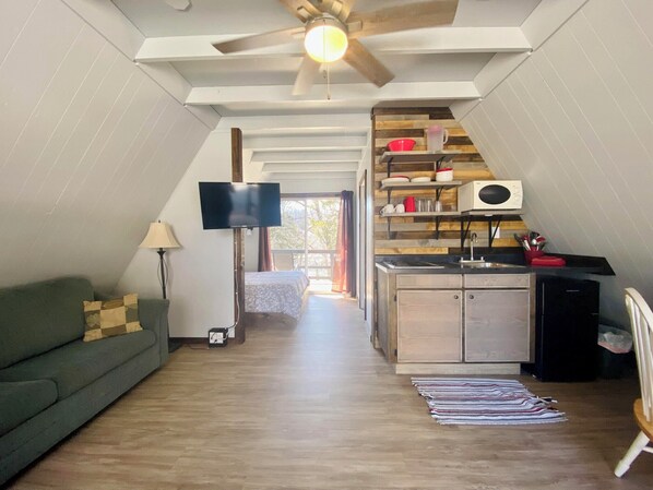 A compact living space with a kitchenette, a flat-screen TV, a ceiling fan, and a sofa.