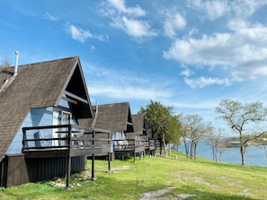 A row of modern cabins with sloped roofs, wooden decks, and large windows, situated by a lake.