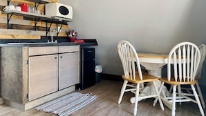Una cocina compacta con microondas integrado, armarios de madera y una zona de comedor con sillas blancas.