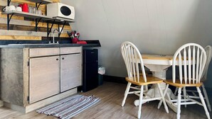 A compact kitchen with a built-in microwave, wooden cabinets, and a dining area with white chairs.