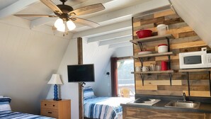A compact bedroom with two beds, a ceiling fan, a TV, and a kitchenette with a microwave and sink.