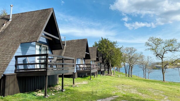 A row of modern cabins with sloped roofs, wooden decks, and large windows, situated by a lake.