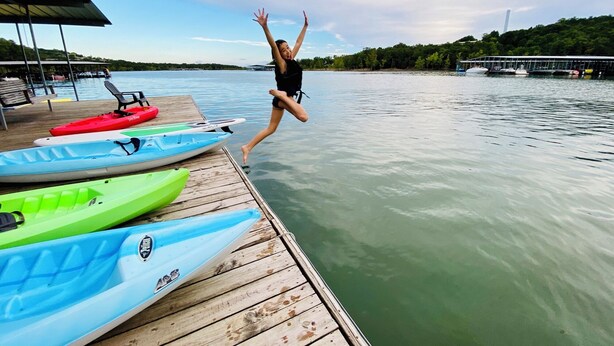 A wooden dock with kayaks and a person jumping into the water.