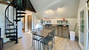 A spacious loft with a wooden dining table, black chairs, a spiral staircase, and a kitchen area with a microwave and stove.
