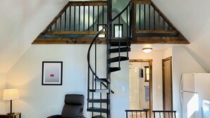 A loft-style room with a wooden staircase, a dining area, and a seating area with a chair.
