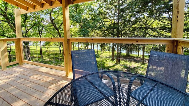 A wooden deck with a metal table and chairs, overlooking a grassy area and trees.
