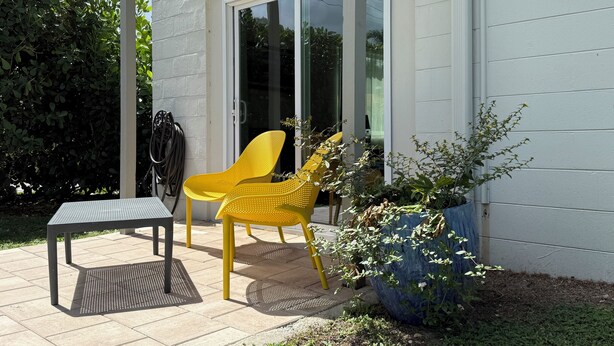 Eine Terrasse mit Tisch und zwei Stühlen, einem großen Blumentopf und einer Schiebetür.