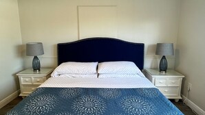 Ein Schlafzimmer mit dunkelblauer Kopfteil, weißer Bettwäsche und zwei Nachttischlampen.