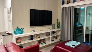 Ein Wohnzimmer mit einem roten Sofa, einem an der Wand montierten Fernseher und einem Regal voller Deko-Objekte.