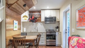 A compact kitchen with white cabinets, a microwave, an oven, and a dining area with a wooden table and chairs. - Cozy & Quiet Retreat ~ Walk to SoCo and Town Lake! (Austin)