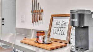 A kitchen counter with a coffee maker, a framed sign that reads "but first COFFEE", and a set of knives on the wall.