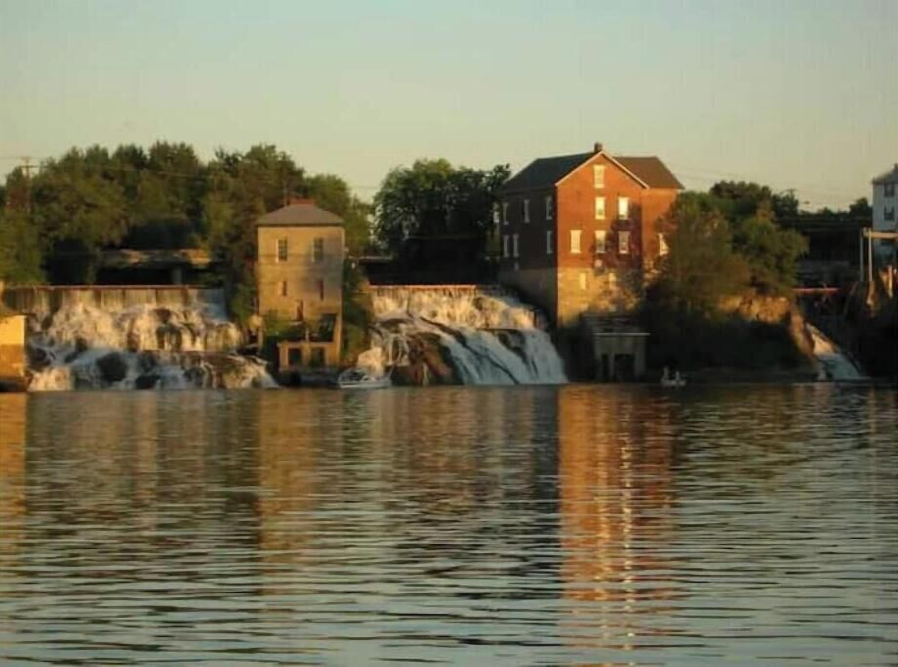 A waterfront property with a waterfall, a boat dock, and several buildings.