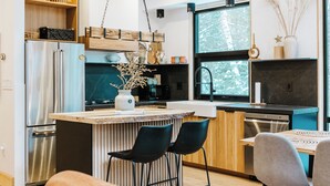 Et moderne køkken med en central ø, rustfrie stålgrebe og et spiseområde med sofa og stole.