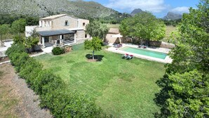 A stone house with a pool, surrounded by a well-maintained lawn and trees, set against a mountainous backdrop. - VILLA VINYA FRARES - LUXURY RETREAT (Pollensa)