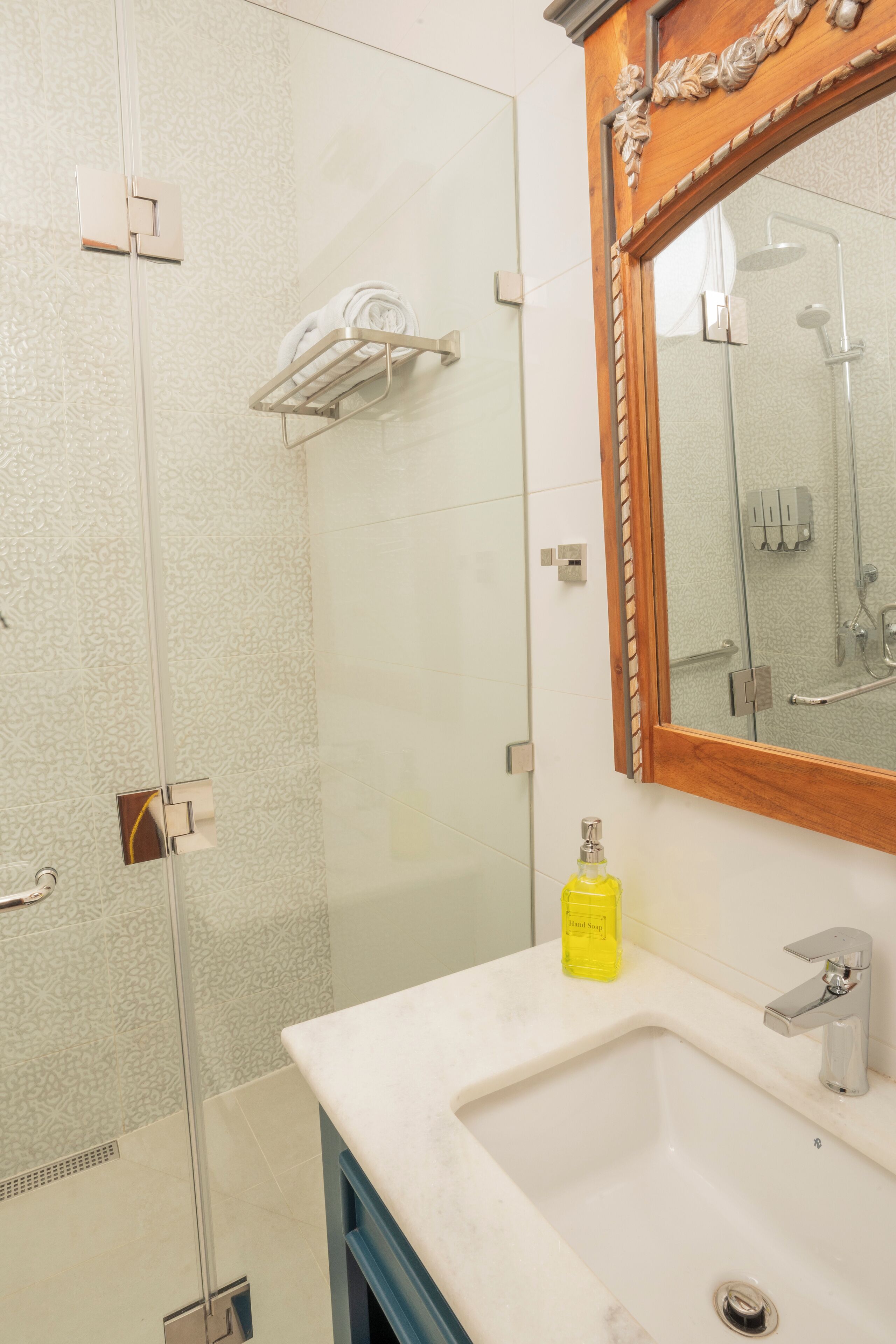 A bathroom with a glass shower enclosure, a white sink with a yellow soap dispenser, and a wooden-framed mirror.