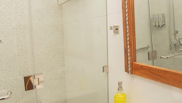 A bathroom with a glass shower enclosure, a white sink with a yellow soap dispenser, and a wooden-framed mirror.